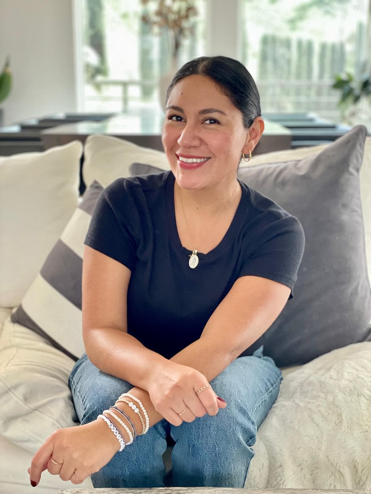 Smiling woman with dark hair in a black t-shirt sits on a white couch.